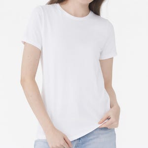 Puede incluir: Una camiseta blanca lisa con cuello redondo y mangas cortas. La camiseta está hecha de un material suave y se usa con vaqueros azules. La camiseta es un básico de vestuario.