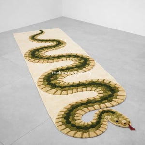 May include: A beige rectangular rug featuring a green and tan snake design. The snake winds across the rug, with a head and red tongue at the end. The text "theloomgallery" is visible on the rug.