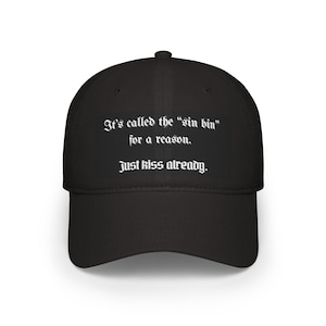 May include: Black baseball cap with the text "It's called the 'sin bin' for a reason. Just kiss already." in white gothic font. The cap has a curved brim and a structured crown.