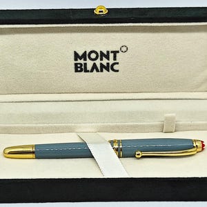 Peut inclure: Un stylo Montblanc dans un coffret noir. Le stylo est gris avec des d&eacute;tails dor&eacute;s et une pointe rouge. Le coffret est doubl&eacute; d'un tissu cr&egrave;me et porte le logo Montblanc.