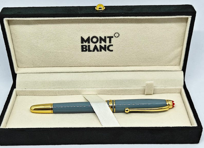 Peut inclure: Un stylo Montblanc dans un coffret noir. Le stylo est gris avec des d&eacute;tails dor&eacute;s et une pointe rouge. Le coffret est doubl&eacute; d'un tissu cr&egrave;me et porte le logo Montblanc.