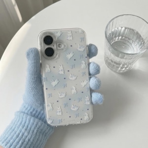 Könnte beinhalten: Transparente Handyhülle mit einem blau-weißen Hasenmuster. Die Hülle wird von einem hellblauen Strickhandschuh gehalten. Ein Glas Wasser steht neben dem Telefon.