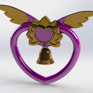 Può includere: Un ciondolo a forma di cuore con una cornice viola e una campana dorata in basso. Il ciondolo presenta un motivo floreale dorato con un cuore viola al centro e ali dorate nella parte superiore.