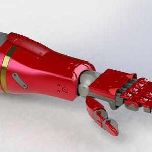 Puede incluir: Un brazo protésico rojo y gris con un acabado metálico. El brazo presenta un antebrazo y una mano rojos, con detalles grises y una banda dorada. Los dedos son articulados, lo que sugiere un diseño funcional.