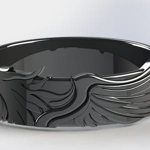 以下が含まれることがあります： 詳細な翼のデザインが施された黒い指輪。滑らかで光沢のある仕上げと幅広のバンドが特徴です。翼のデザインが指輪を包み込み、大胆でエレガントな外観を作り出しています。指輪はおそらく金属製です。