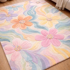 May include: A large, rectangular rug with a floral design. The rug features large, pastel-coloured flowers in pink, orange, yellow, and purple, set against a cream-coloured background with wavy patterns. The rug is made of a soft, plush material.