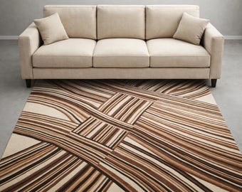Può includere: Un divano beige con due cuscini abbinati è posizionato sopra un tappeto rettangolare. Il tappeto presenta uno sfondo color crema con strisce marroni e beige che si intersecano, creando un motivo geometrico moderno. Il tappeto è progettato per completare il divano.