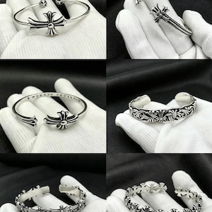 May include: Silver bracelets featuring cross and floral patterns. The bracelets are shown on a white surface. Designs include a central cross, crosses at the ends, and a repeating floral motif. The bracelets are made of a shiny metal.