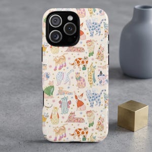 May include: A smartphone case with a cream-colored background featuring a repeating pattern of illustrated cats in various poses, colors, and outfits, including cats with floral prints, wings, hats, and accessories, interspersed with small star shapes.