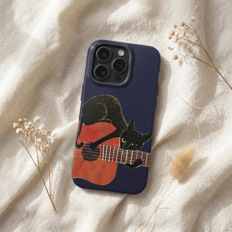 May include: A dark navy blue smartphone case featuring a graphic illustration of a black cat resting on an orange acoustic guitar. The cat has yellow eyes and is positioned across the guitar neck and body. The case has a triple camera cutout.