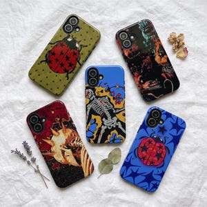 May include: Five rectangular smartphone cases featuring distinct graphic designs. One case is olive green with a ladybug, one is black with abstract red and orange patterns, one is blue with a skeleton, one is red with a skull, and one is blue with a ladybug.