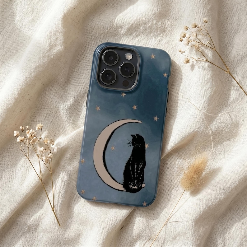 May include: A dark blue smartphone case featuring a graphic illustration of a black cat sitting on a crescent moon against a starry night sky background. The case has a cutout for a triple-lens camera system on the upper left corner.