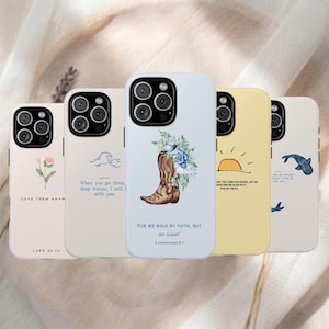 May include: Five smartphone cases featuring various designs and scripture verses. The cases display a flower with 'LOVE THEM ANYWAY', a wave with 'When you go through deep waters', a cowboy boot with 'FOR WE WALK BY FAITH, NOT BY SIGHT', a sun with 'PSALM 118:24', and a whale.