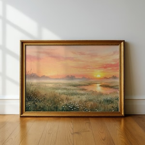 Puede incluir: Pintura de paisaje enmarcada que representa un amanecer sobre una marisma. La obra de arte presenta un marco dorado, un río y un cielo vibrante con tonos naranja, rosa y amarillo. El primer plano muestra hierba alta y flores silvestres.