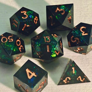 Puede incluir: Juego de siete dados poliédricos con un acabado oscuro e iridiscente. Los dados tienen números y bordes de color cobre. Los colores incluyen verde oscuro, azul y negro. Estos dados son para juegos de mesa.
