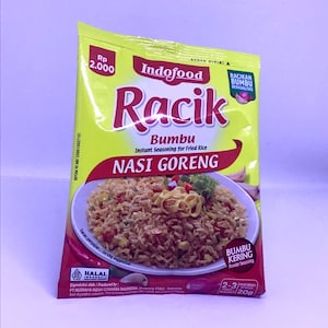 Może przedstawiać: Żółto-czerwone opakowanie Indofood Racik Bumbu Nasi Goreng, przyprawy instant do smażonego ryżu. Opakowanie zawiera obraz smażonego ryżu i tekst w języku indonezyjskim. Opakowanie zawiera również tekst "HALAL INDONESIA".