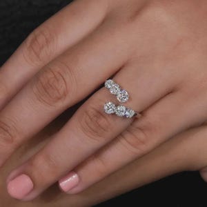 May include: A silver ring featuring two rows of sparkling diamonds. The ring wraps around the finger, with three diamonds on one side and two on the other. The diamonds are clear and brilliant, set against a silver band.