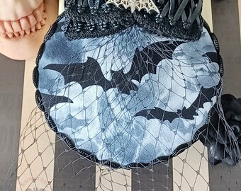 May include: A black and blue Halloween-themed headpiece with a bat and cloud pattern. The headpiece features a black net veil, a decorative bat, and a black beaded trim. The fabric has a bat and cloud design.