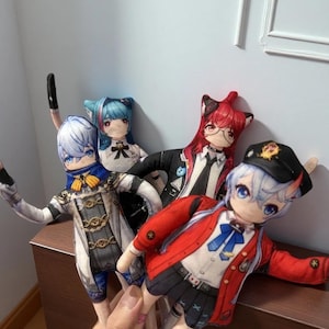 May include: Four anime-style plush dolls with cat ears. The dolls have detailed outfits in various colors, including red, blue, and black. One doll wears a red jacket and a black cap. The dolls are held by a hand.