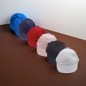 May include: Six baseball caps in a row, each in a different colour: bright blue, navy, red, pale pink, black, and light grey. The caps are displayed diagonally, highlighting their diverse shades and designs. The caps are made of a soft material.
