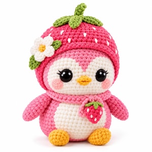 May include: A crochet plush toy shaped like a penguin wearing a pink strawberry hat with a green stem and a white flower. The penguin has a white face, black eyes, a yellow beak, pink cheeks, a pink scarf, and a small strawberry charm.