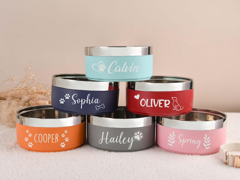 Puede incluir: Seis cuencos personalizados para mascotas, apilados. Cada cuenco tiene un borde plateado y un color diferente: naranja, azul marino, rojo, gris, azul claro y rosa. Nombres y huellas de patas.