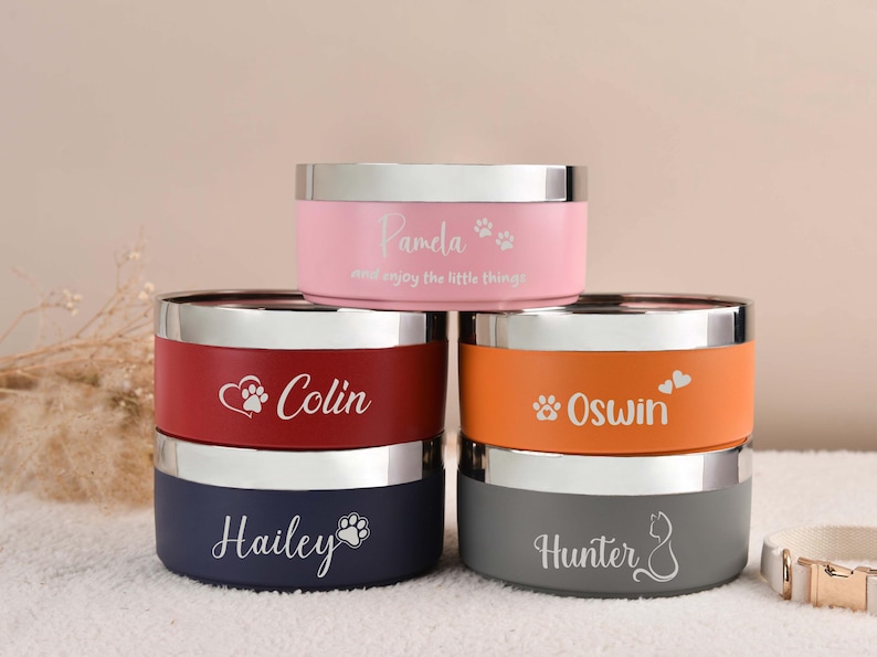 Puede incluir: Un conjunto de cuencos personalizados para mascotas en rosa, rojo, naranja, azul marino y gris con bordes plateados. Cada cuenco est&aacute; grabado con el nombre de una mascota y un dise&ntilde;o de huella de pata o coraz&oacute;n. El cuenco rosa dice "Pamela".