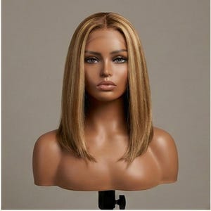 Peut inclure: Perruque blonde de style bob avec des mèches, présentée sur une tête de mannequin. La perruque présente une ligne de cheveux naturelle et une coupe droite. La couleur des cheveux est un mélange de tons brun clair et blond.