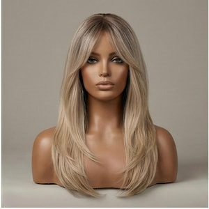 Puede incluir: Peluca rubia con cabello en capas, largo hasta los hombros y flequillo. La peluca se muestra en una cabeza de maniquí con un fondo neutro. El cabello tiene una raíz oscura y se desvanece a un rubio más claro.