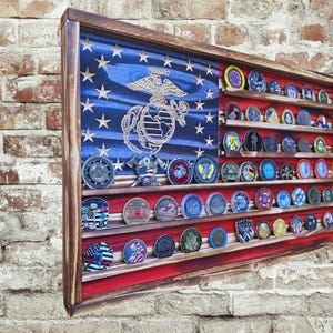 May include: Wooden display case in the shape of an American flag, with a blue field of stars and red stripes. The case is designed to hold challenge coins, with multiple shelves. The case has a dark brown wooden frame.