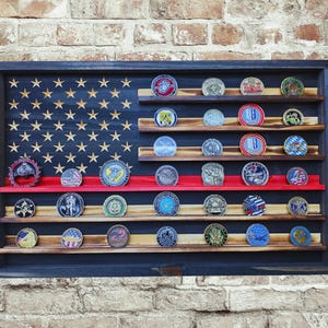 May include: A wooden coin display case shaped like the American flag. The case has a dark blue frame, a wooden flag design with stars, and shelves holding various coins. A red stripe is visible.