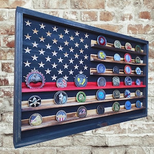 May include: A wooden display case shaped like the American flag, with a blue frame and a red stripe. The case is filled with various challenge coins on wooden shelves. The flag design features white stars and stripes.