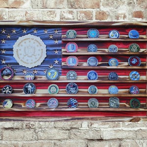 May include: Wooden display case shaped like an American flag, with red and white stripes and a blue field with stars. The case holds numerous challenge coins on wooden shelves, with a Department of Justice emblem in the center.