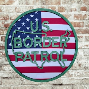May include: A round wooden sign with a green border and the text "U.S. BORDER PATROL". The sign features the American flag design with red and white stripes and a blue field with white stars. The text is in green.