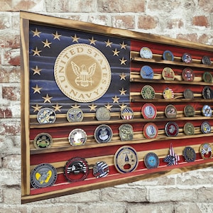 May include: Wooden display case in the shape of an American flag, featuring a blue field with stars and red and white stripes. The case holds various military challenge coins, with a large United States Navy emblem.