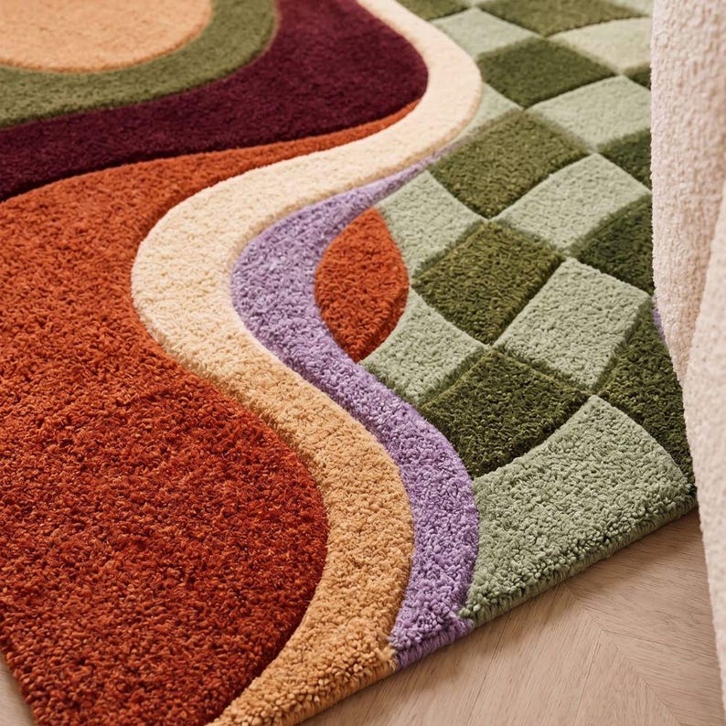 May include: A tufted area rug featuring a combination of patterns, including large flowing curves in shades of rust orange, deep burgundy, cream, and lavender, alongside a section of green and light green checkered square blocks.