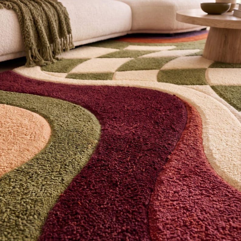 May include: A textured area rug featuring a pattern of wavy, curved bands in shades of deep burgundy, olive green, and cream. The rug has a thick, tufted pile construction with distinct color-blocked sections that create a flowing, organic design.