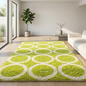 May include: A rectangular, lime green shag rug with a repeating pattern of large white circles. The rug is placed on a hardwood floor in a modern living room setting, with a white sofa and large windows.
