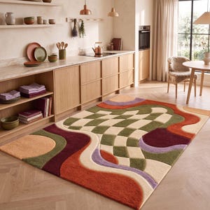 May include: A rectangular area rug featuring a tufted texture with a central checkered pattern in olive green and cream. The design includes wavy, organic shapes in shades of burnt orange, deep burgundy, lavender, and tan, creating a layered effect.