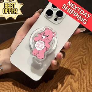 May include: A pink Care Bear phone grip with the text "PLEASE SHUT THE FUCK UP" on a white circle. The grip is attached to a silver phone. The image also includes a "BEST OFFER" and "NEXTDAY SHIPPING" banner.