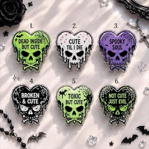 May include: Six heart-shaped skull pins with dripping edges and spiderweb details. The pins feature text: 1. DEAD INSIDE BUT CUTE, 2. CUTE TIL I DIE, 3. SPOOKY SOUL, 4. BROKEN & CUTE, 5. TOXIC BUT CUTE, 6. NOT CUTE JUST EVIL in various color schemes.