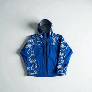 May include: A bright blue hooded jacket with a full-length zip and two front pockets. The jacket has a white, stylized graphic pattern across the shoulders and sleeves. The jacket is designed for outdoor activities.