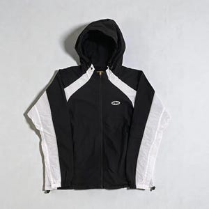 May include: Black hooded jacket with white panels on the sleeves and shoulders. The jacket features a full-length zip and a small logo on the chest. The lightweight jacket is suitable for layering and measures approximately 70 cm in length.
