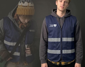 May include: A navy blue zip-up vest featuring two horizontal reflective silver stripes and a white logo on the chest that reads Lightfoot Medical Transport. The vest is worn over a grey hooded sweatshirt and a yellow plaid shirt.