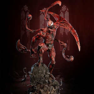 Puede incluir: Estatua roja y negra del personaje Carnage de Marvel Comics, de pie sobre una lápida. La estatua tiene un físico muscular detallado, con zarcillos y una expresión amenazante. El fondo presenta un entorno oscuro de estilo gótico.