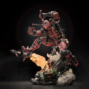 Könnte beinhalten: Eine dynamische Deadpool-Statue in einem rot-schwarzen Anzug, mit einem Schwert und einer Pistole, sowie einer Rakete. Die Figur ist in einer dynamischen Pose, auf einem detaillierten Sockel mit einer feurigen Explosion und dem Wort "BOOM".