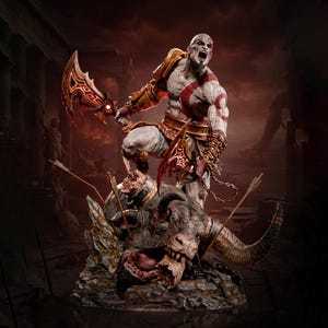 May include: A detailed figurine of a pale, muscular warrior with a red tattoo, standing over a defeated bull-like creature. The warrior holds two ornate, glowing blades with chains attached to the arms, wearing gold armour and brown leather accents.