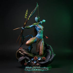 May include: A detailed figurine of a Na'vi warrior from the Avatar movie, poised with a bow and arrow. The figure is blue with intricate body markings, wearing tribal attire, and set on a base with detailed plant life. The text "Alpha3DEmpire" is at the base.