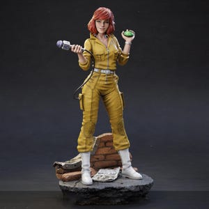 May include: A figurine of a character in a yellow jumpsuit, holding a microphone and a green object. The figure has red hair and white boots. The figure is standing on a stone base with brick and a newspaper.