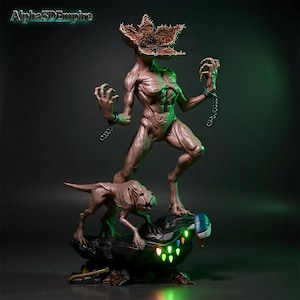 May include: A detailed brown Demogorgon statue from the Stranger Things series, with a smaller creature at its base. The Demogorgon has a flower-like head and is chained. The base has glowing green lights and the text "Alpha3DEmpire".